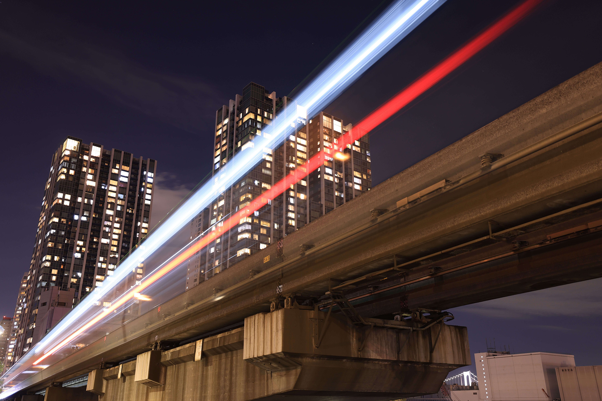 Light trails above an elevated concrete bridge with lit-up high rises in the background, photographed with the Canon EOS R5