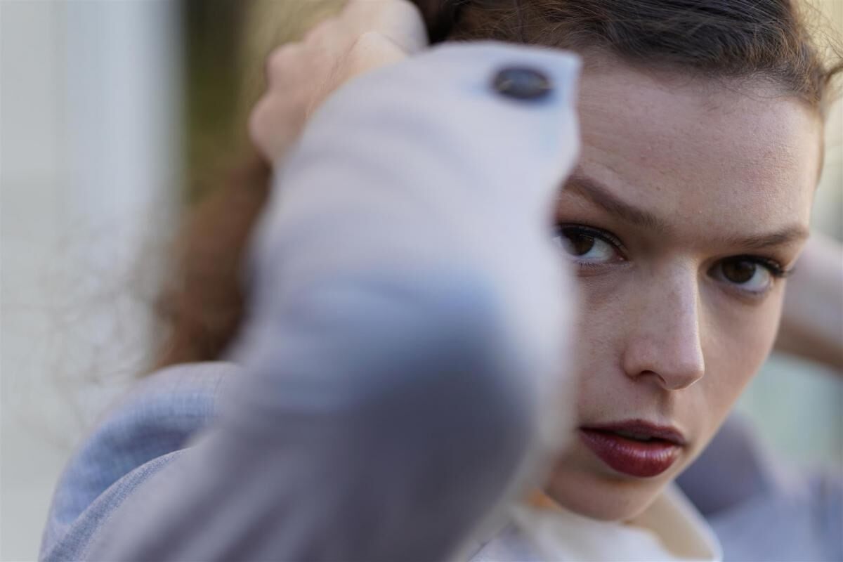 Young woman with brown eyes gazing intently ahead while holding her hair, photographed with the Sony a7III mirrorless camera