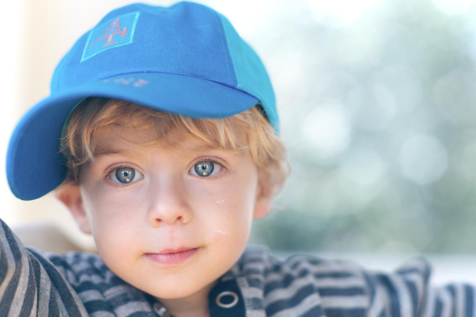 Blonde-haired, blue-eyed boy wearing a blue cap and striped top, photographed with the Nikon AF-S NIKKOR 85mm f/1.4G Lens