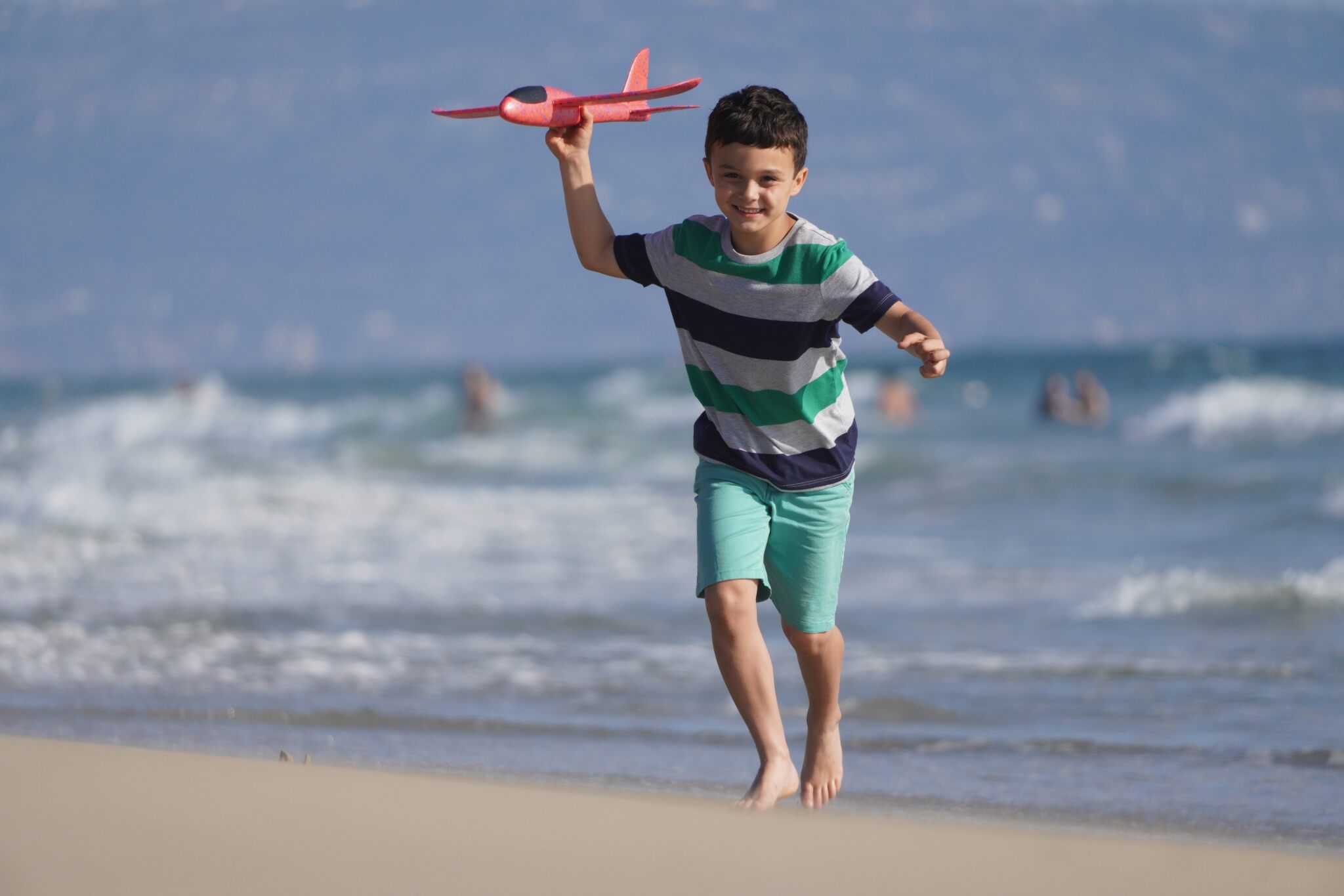 Boy in striped T-shirt running along beach with toy the plane in hand, shot using the Sony E 70- 350mm f4.5-6.3 G OSS Lens