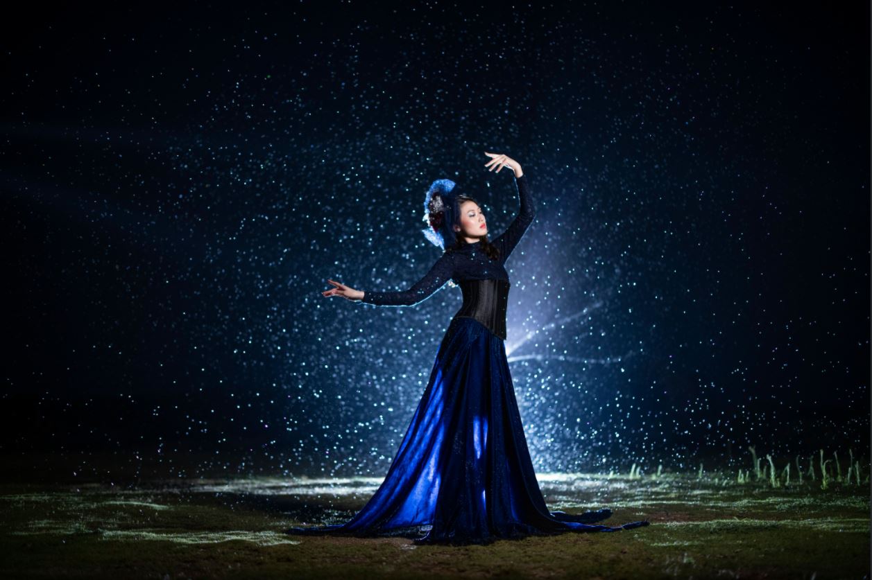 Fashion model in dark blue gown posing in front of a burst of white dots, photographed using the Canon Speedlite EL-1