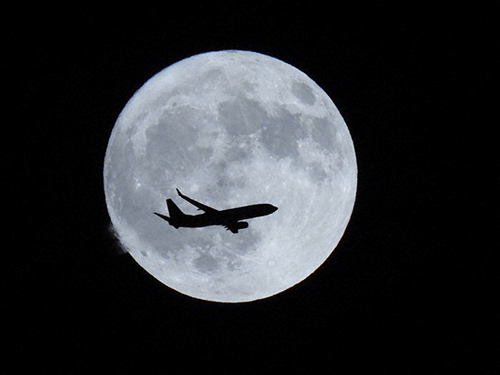 Aeroplane silhouetted against a much larger moon, photographed using the Nikon Coolpix P950