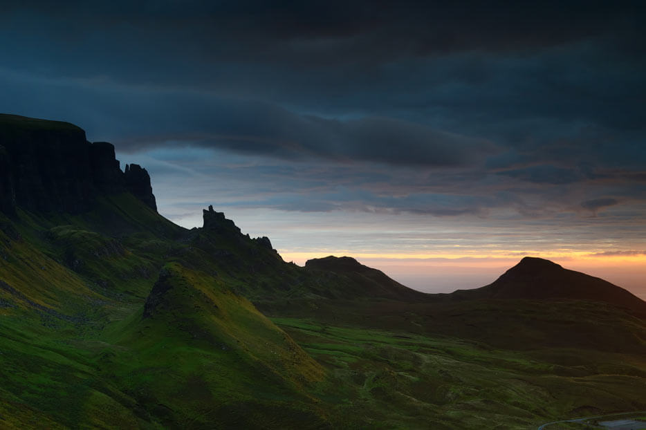 Dark, jagged green landscape beneath dark clouds and a hint of sunset, photographed with the Nikon 50mm 1.8G lens