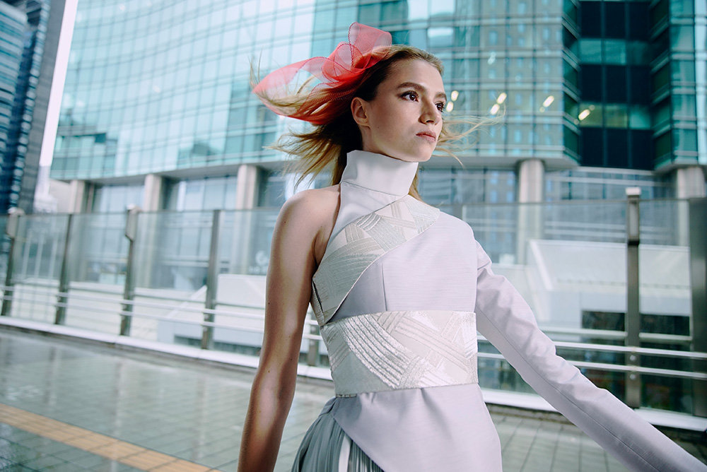 Young woman in futuristic white outfit walking past steel and glass buildings, shot with the Sony a7s III 