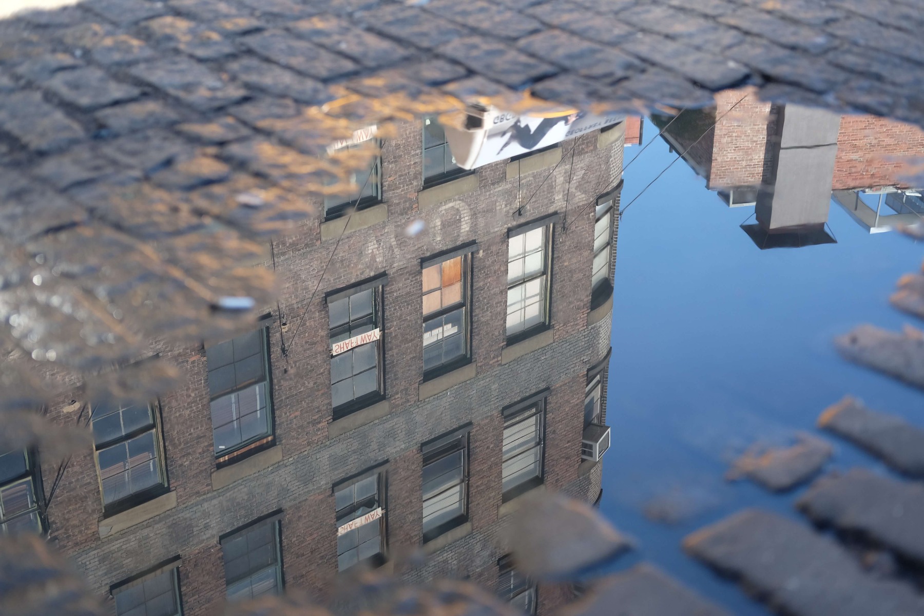 Old brick building reflected in a puddle on a cobbled street, photographed with the Fujifilm XF 35mm f/2 R WR Lens