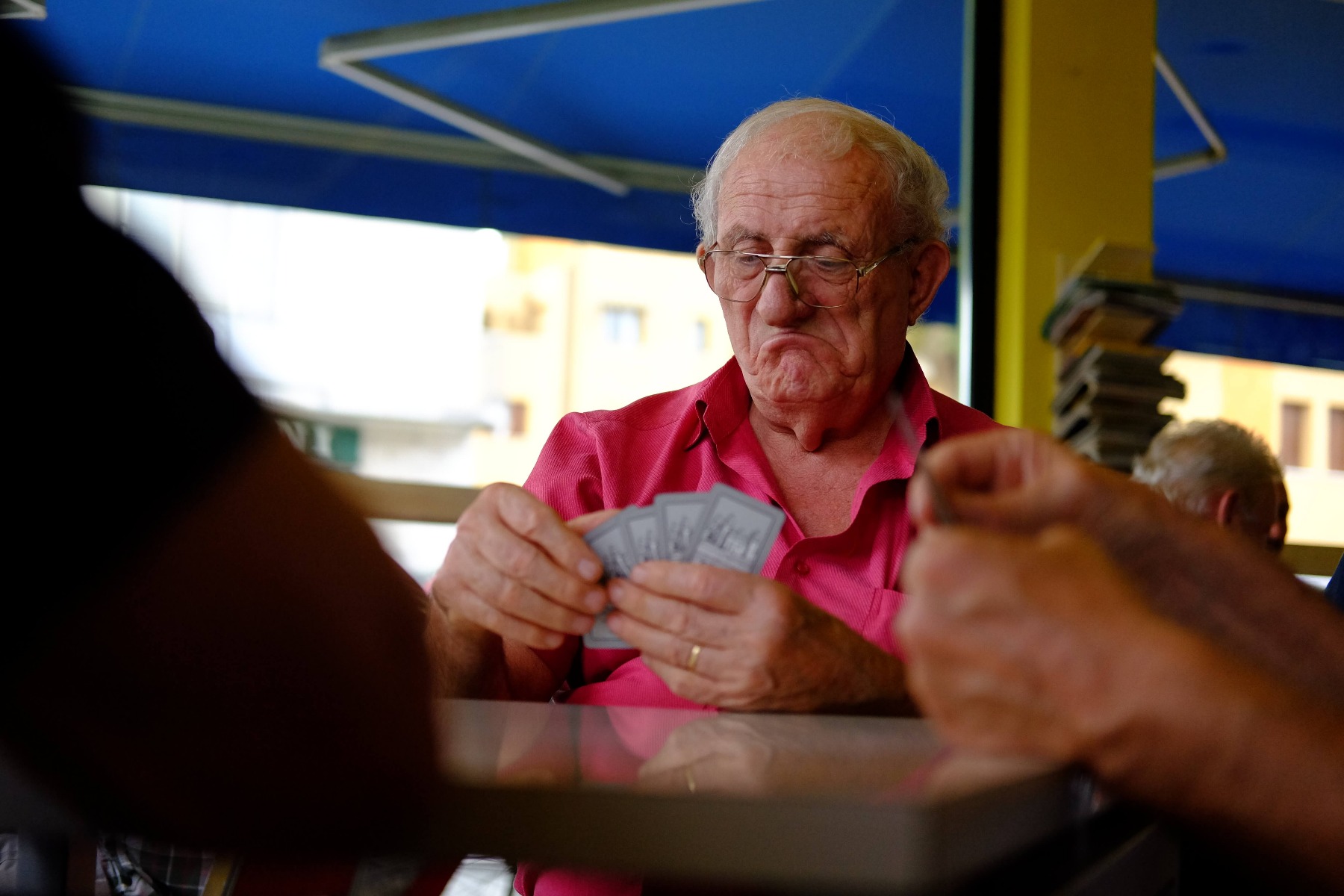 Old man in glasses frowning while playing cards with friends, photographed with the Fujifilm XF 35mm f/2 R WR Lens