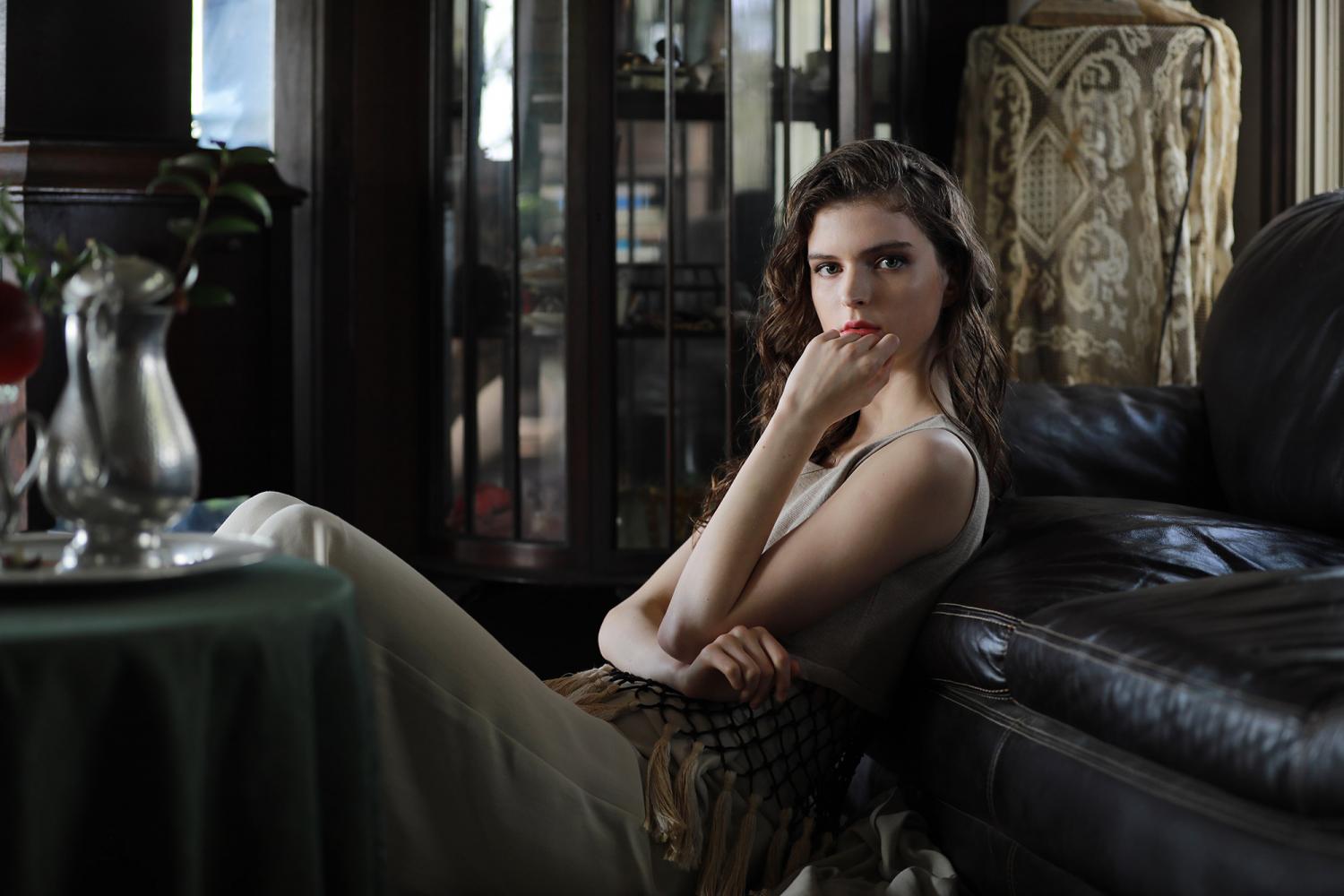 Long-haired young woman in elegant dress reclining against a leather couch, photographed with the Canon 70-200mm f2.8L IS III