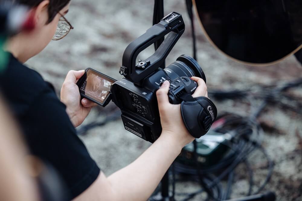 Filmmaker monitoring the flip-out screen of the Canon EOS C70 cinema camera 