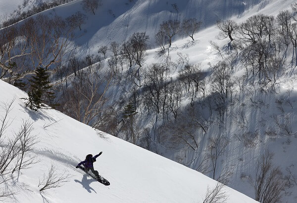 Figure snowboarding down a slope backdropped by tree-covered mountains, shot with Canon RF 100-500mm f4.5-7.1 L IS USM Lens