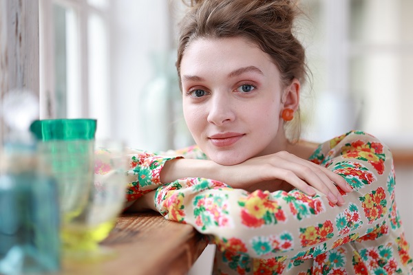 Smiling young woman in floral top resting on the edge of a wooden table, shot with the Canon RF 85mm f2 Macro IS STM lens