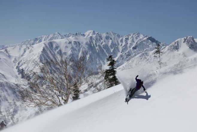 Figure snowboarding downhill with trees and snow-covered mountains in the background, photographed with the Canon EOS R5