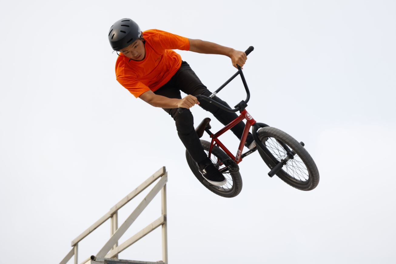 Bike rider in helmet and orange T-shirt suspended mid-air against an overcast sky, photographed with the Canon RF 70-200mm f4 L IS USM lens