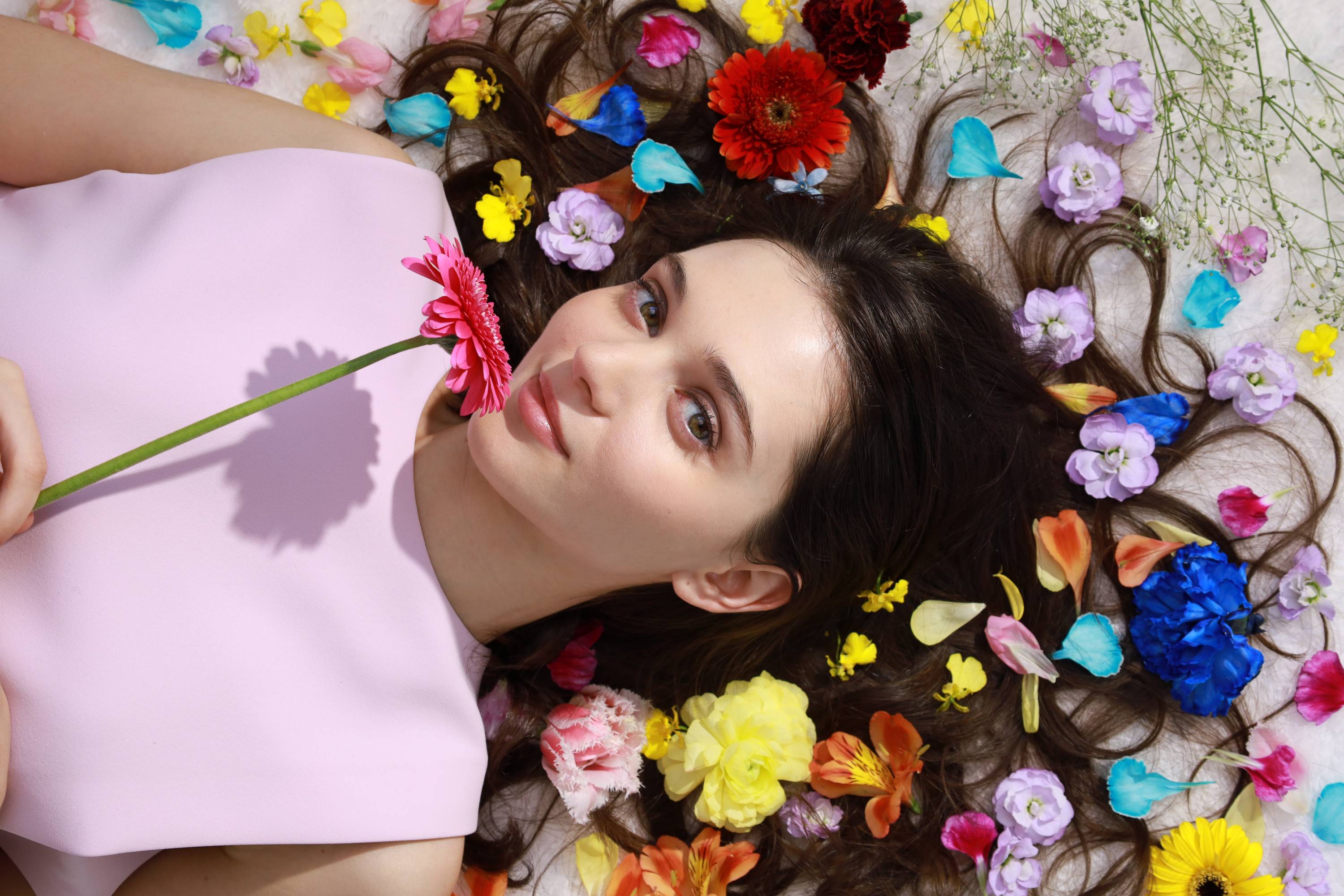 Young woman holding a pink flower while surrounded by different coloured flowers, shot with Canon RF 24-105mm f/4-7.1 IS STM lens