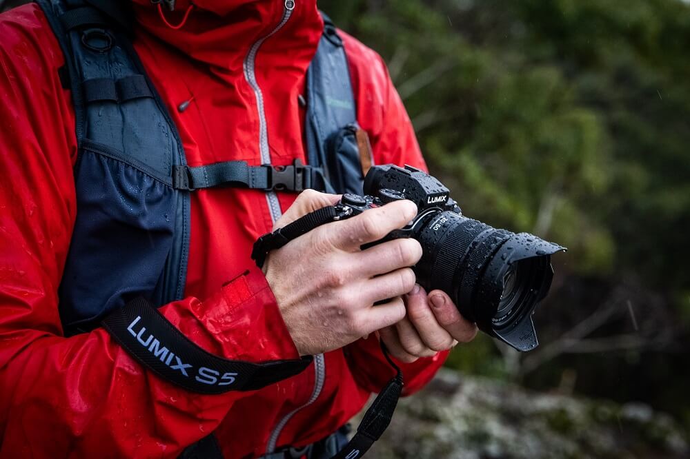 Man in a wet red windbreaker holding a Panasonic Lumix S5