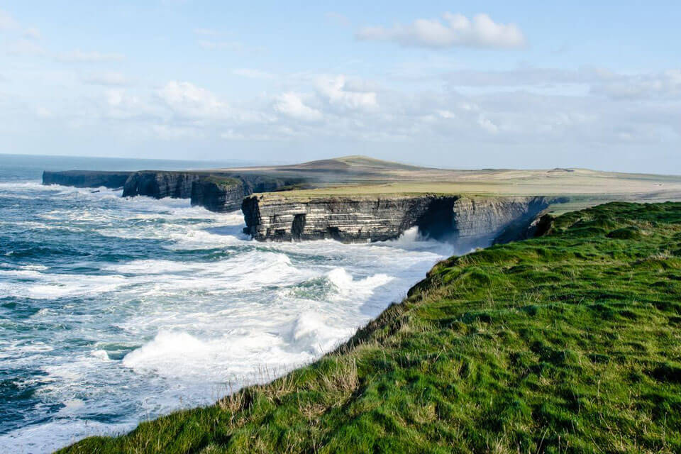 View from grassy clifftop towards ocean waves and cliffs in the distance, photographed with the Nikon AF-S DX NIKKOR 35mm f/1.8G lens