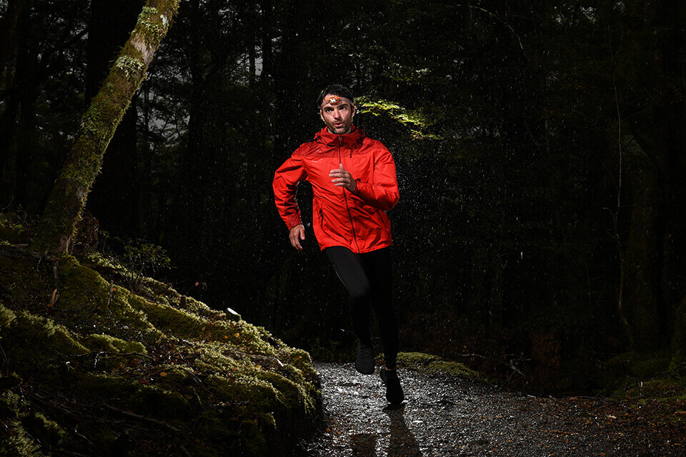 Man, wearing an orange jacket, jogging through a forest at night – photographed with the Nikon D7500 DSLR camera