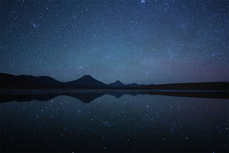 Mountains beneath starry sky reflected in water, shot in the Atacama Desert with the Nikon Z 20mm f/1.8 S lens