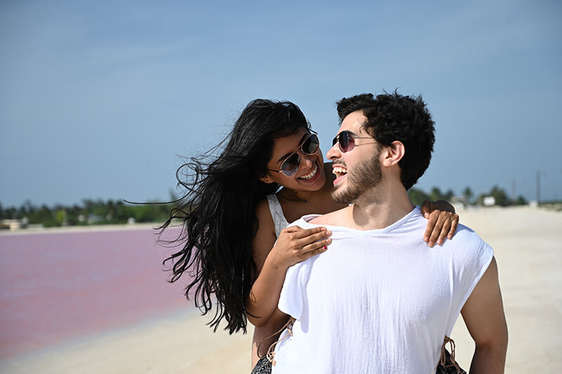 Happy couple in sunglasses laughing beside a pink lake in Mexico, photographed with the Nikon NIKKOR Z 24-70mm f/4 S Lens