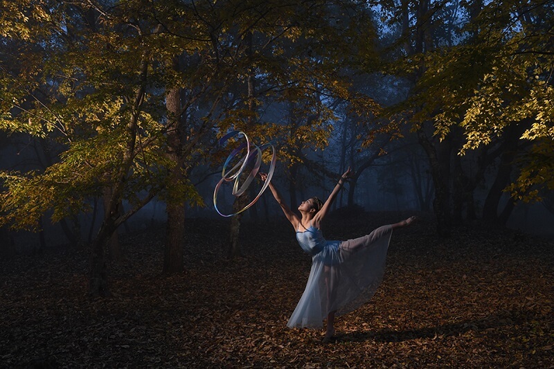 Ballerina on tiptoe, twirling a coloured ribbon amidst a misty forest, photographed using the Nikon SB-5000 flash