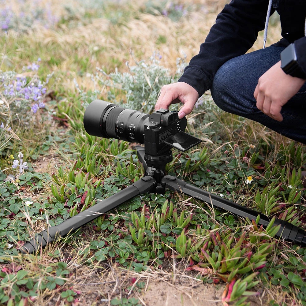 Man operating a Sony camera and telephoto lens on the Peak Design Travel Tripod set up close to the ground