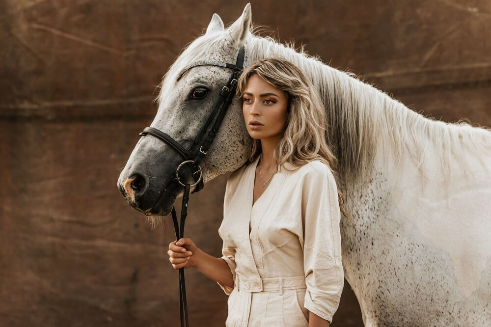 Woman in white outfit holding the reins of a white horse resting its head on her shoulder, shot with the Profoto A10