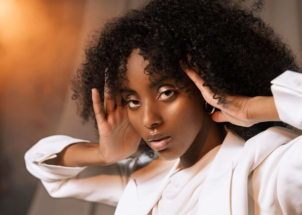 Close-up of fashion model in white jacket holding her hands against the sides of her face, photographed with the Profoto A10