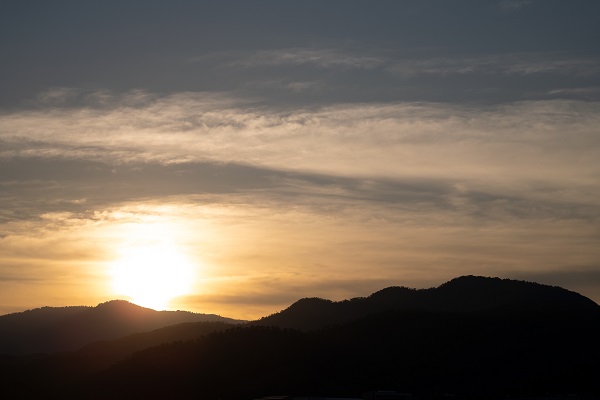 Sun setting behind silhouetted hills under a cloudy sky, photographed with the Sigma 105mm f2.8 DG DN Macro Art lens 