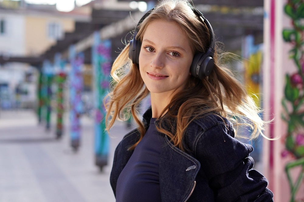 Smiling young woman wearing headphones as her hair blows in the wind, photographed with the Sony a6400