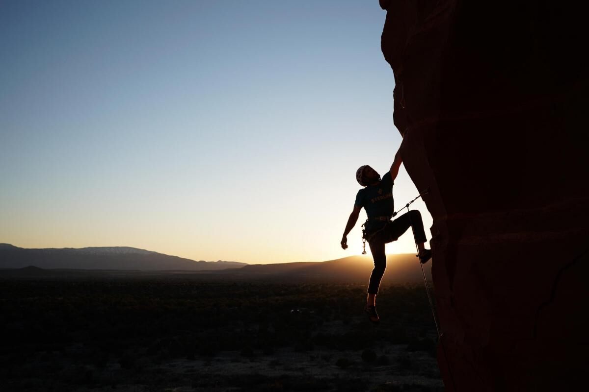 Rock climber scaling a cliff, silhouetted by the sun on the horizon – photographed with the Sony 16-35mm f2.8 GM Lens