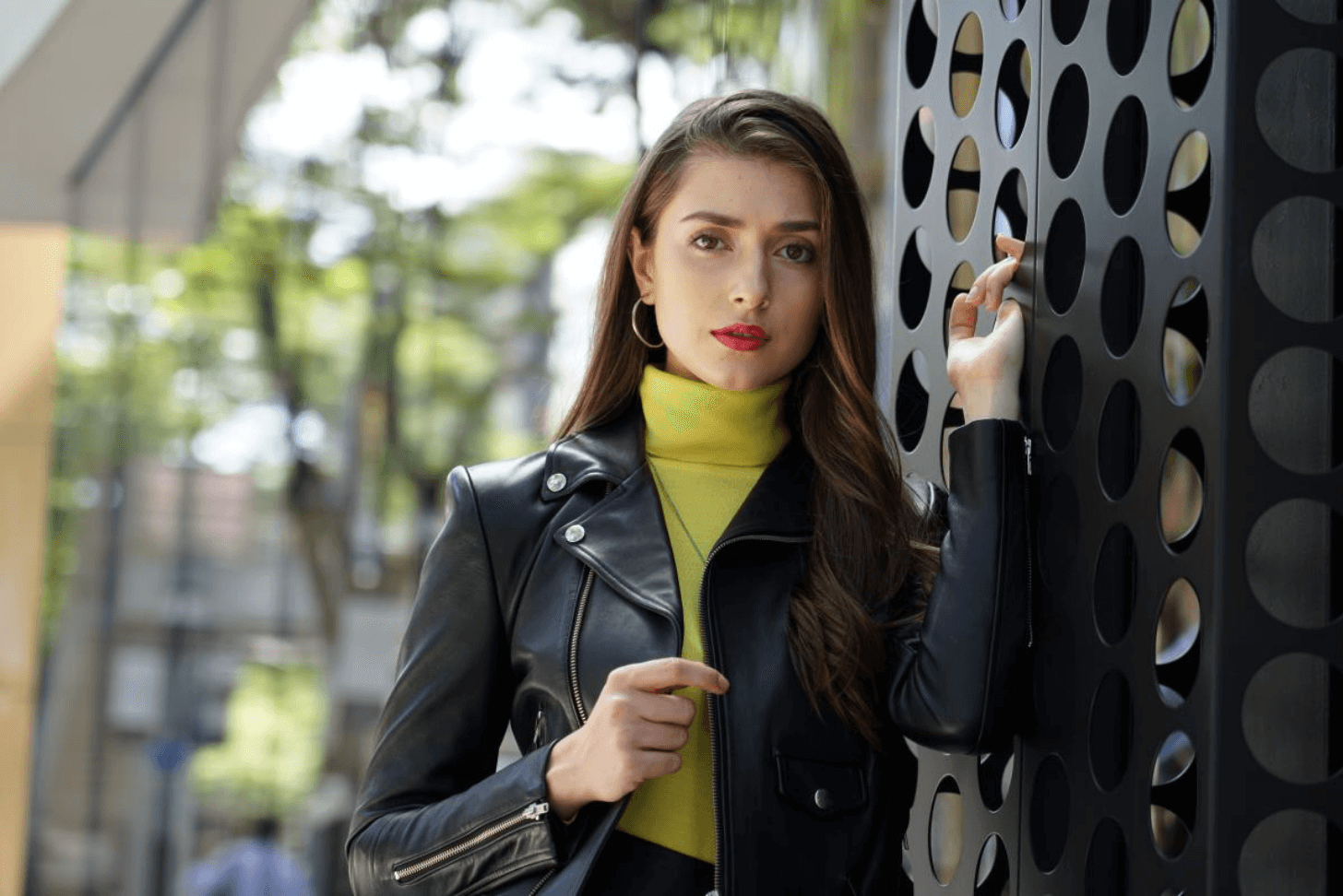 Young long-haired woman in leather jacket posing against a modern building, photographed using Sony 24-105mm f/4 G OSS Lens