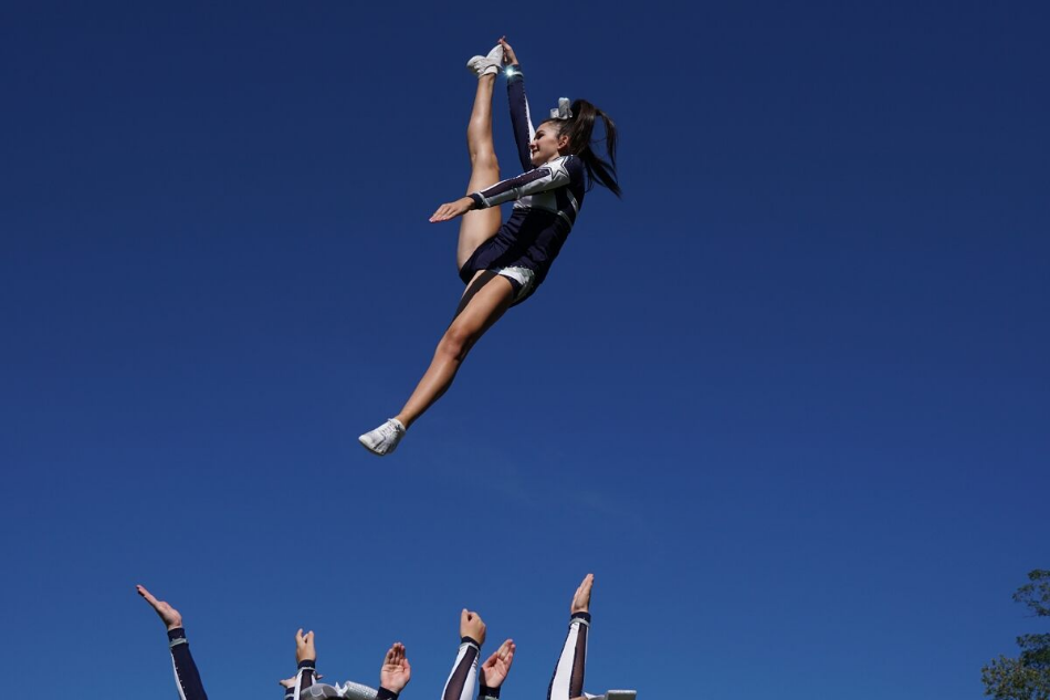 Cheerleader doing the splits mid-air above other cheerleaders preparing to catch her, shot with Sony FE 24-70mm f/2.8 GM Lens