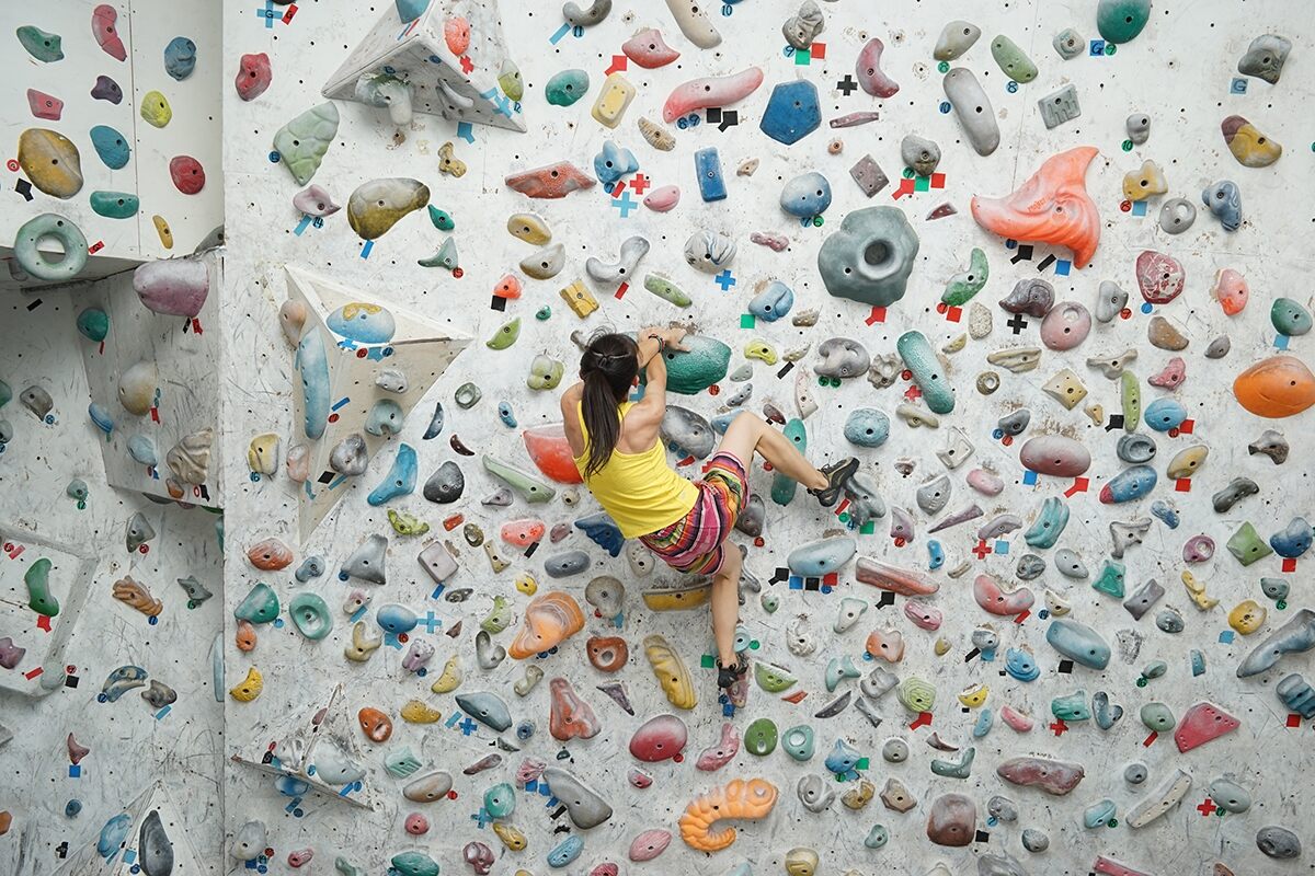 Woman indoor rock climbing up a wall of colourful grips, photographed with the Sony FE 28-70mm f/3.5-5.6 OSS lens