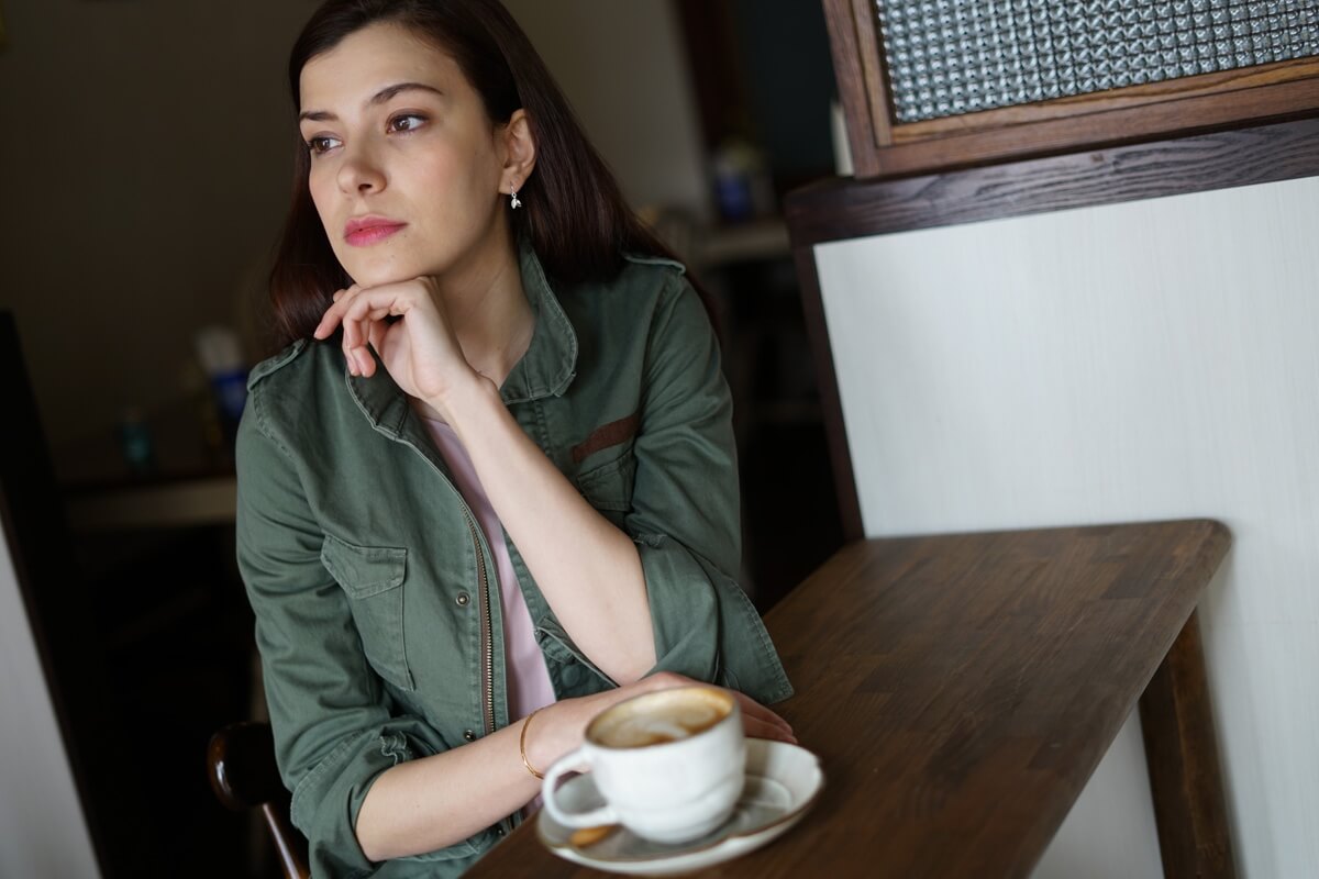 Young woman with dark hair sitting at a wooden table, beside a cup of coffee – photographed with the Sony 50mm f1.8 lens