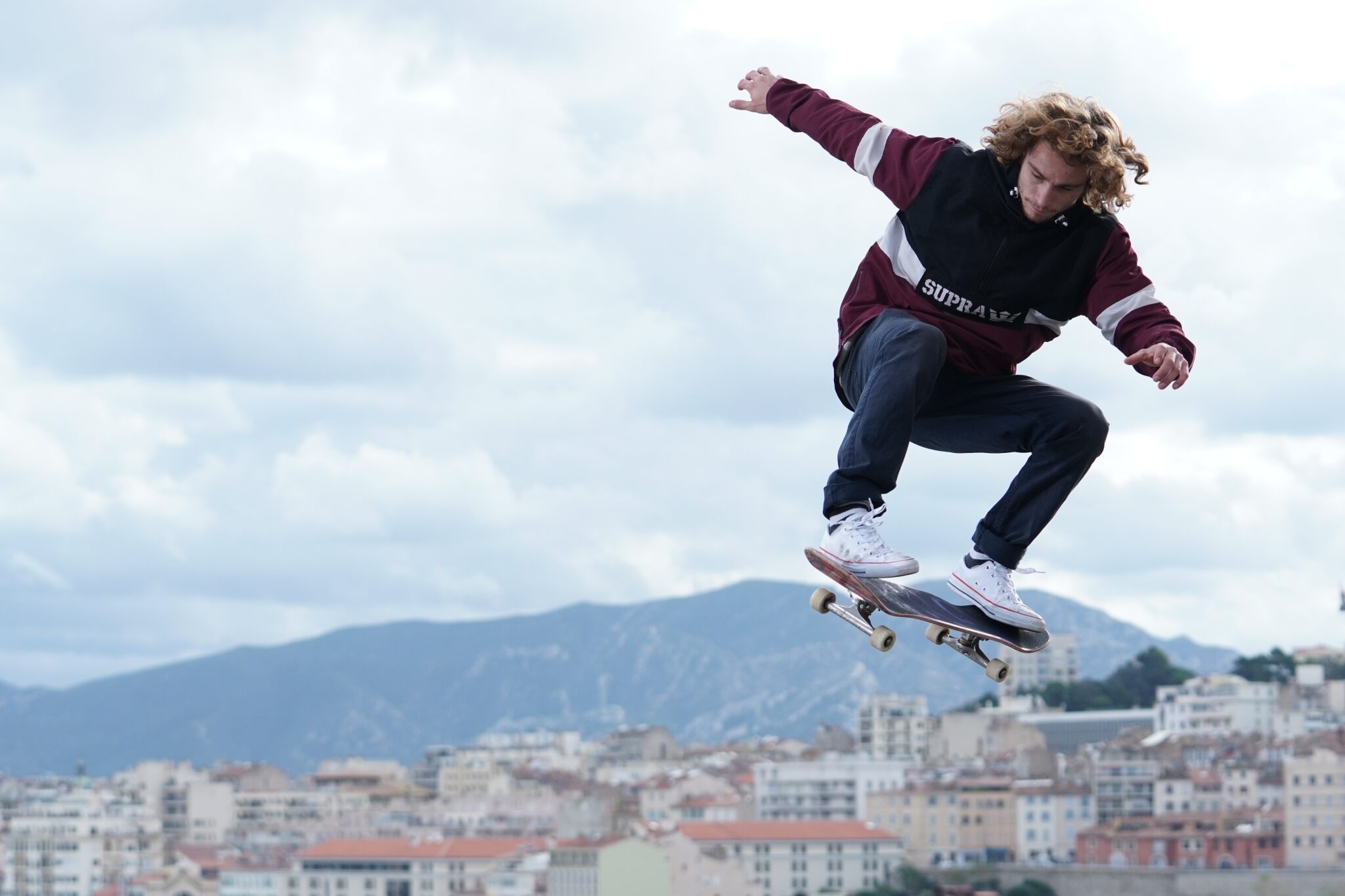 Young man skateboarding mid-air against a backdrop of buildings & mountains, shot with the Sony FE 70-200mm f/2.8 GM OSS lens