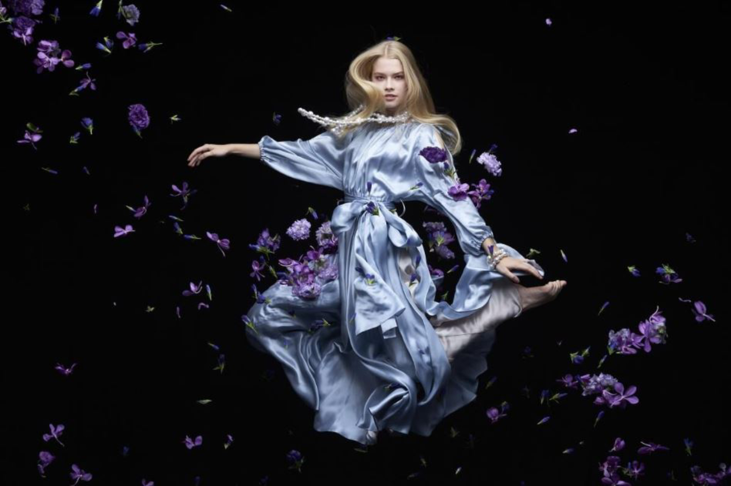 Blonde woman in flowing blue dress floating amidst purple flowers, photographed with the Sony 85mm f1.4 GM lens