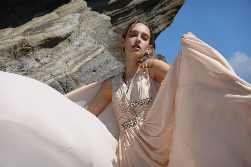 Female fashion model wearing a billowing beige dress in front of large rocks, photographed from with the Sony RX100 VII