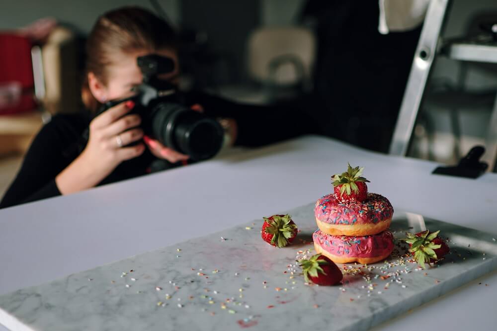 Female photographer doing a food photography shoot of doughnuts and strawberries