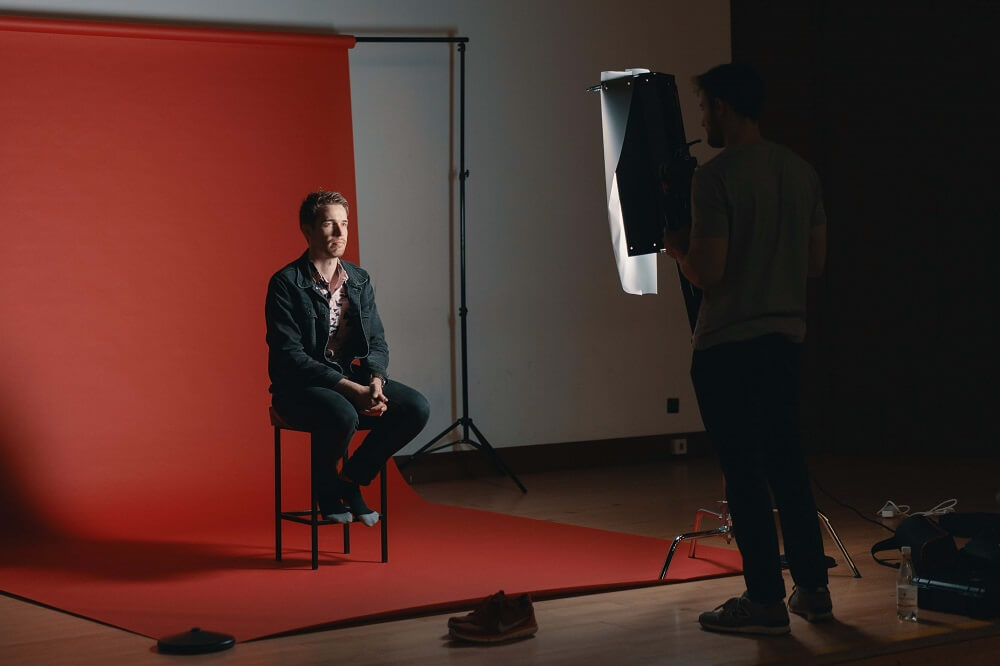 Male model sitting in a photo studio with a red backdrop