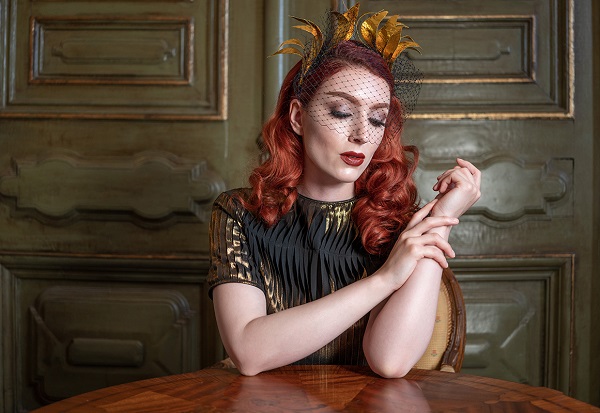 Red-haired woman wearing gold headpiece gazing at the table on which her elbows rest, shot with the Tamron 35mm f2.8 Sony lens