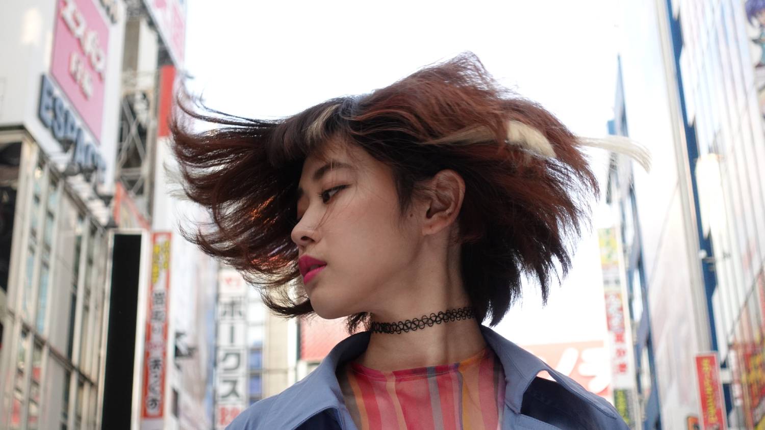 Young woman turning to the side, hair swishing in the air, with Tokyo buildings in the background, shot on the Sony ZV-1