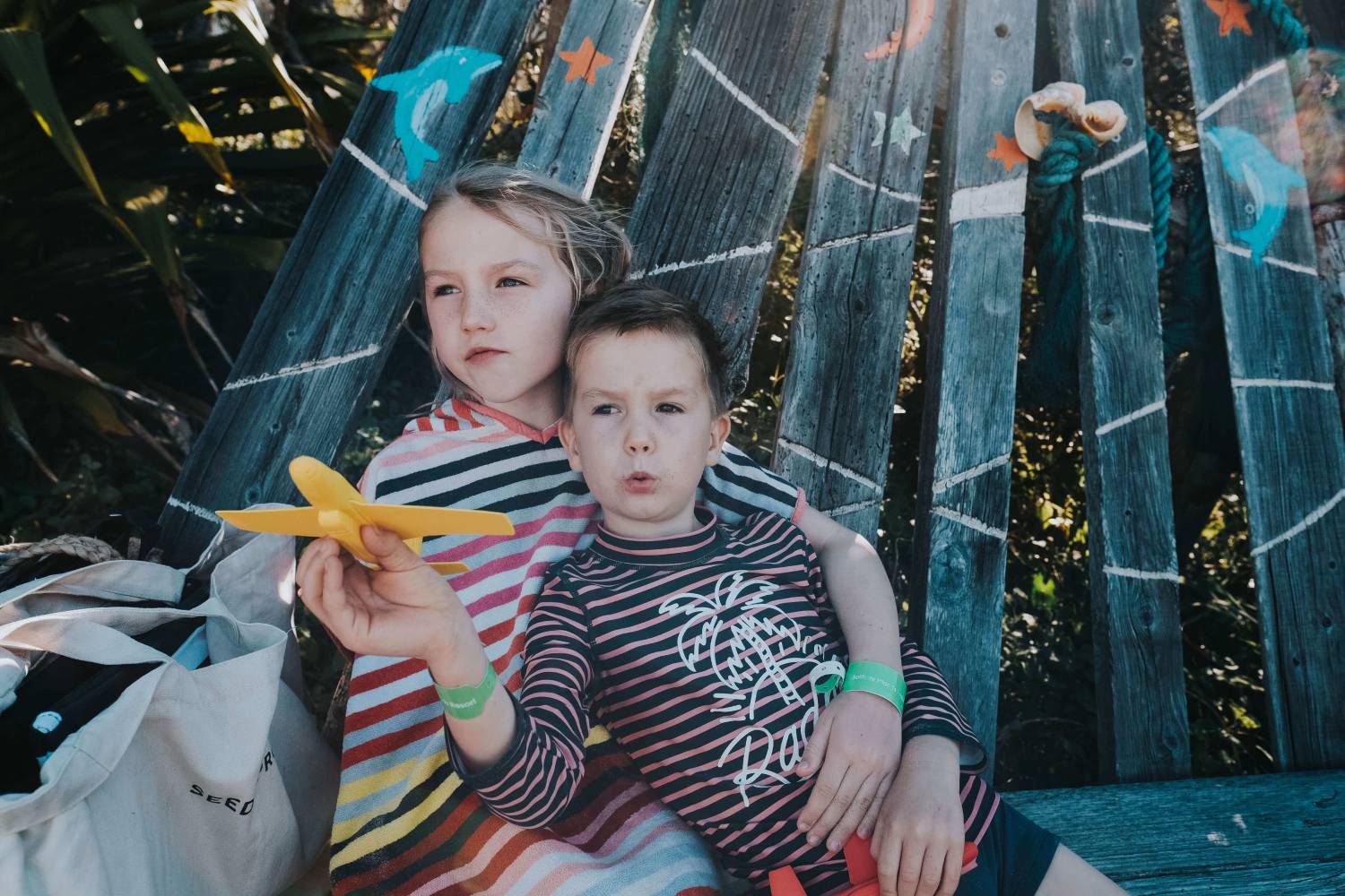 siblings sitting on a chair while holding a toy airplane