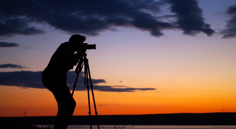 silhouette of a man with a camera and tripod shooting during sunset