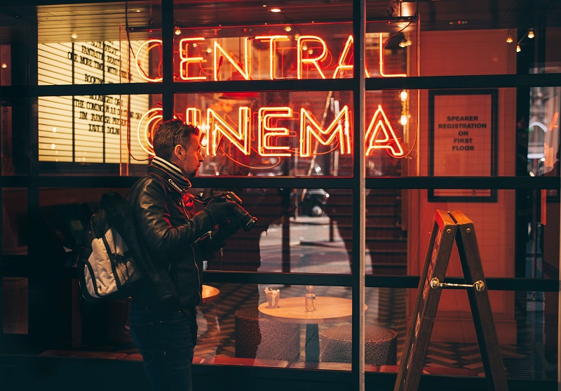 man outside of a brightly lit store, taking street photos