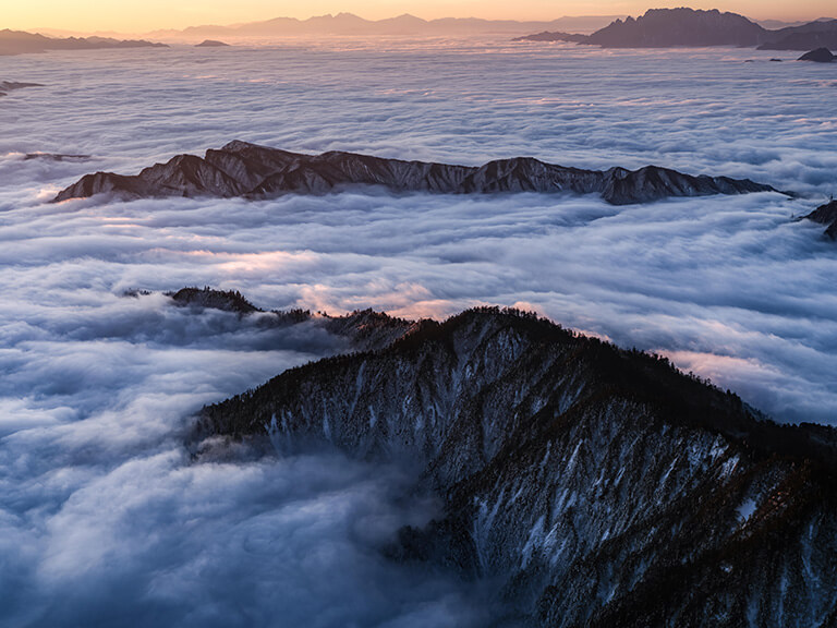 Wave-like clouds surrounding mountains under an orange-tinged sky, photographed with the Fujifilm GFX100s