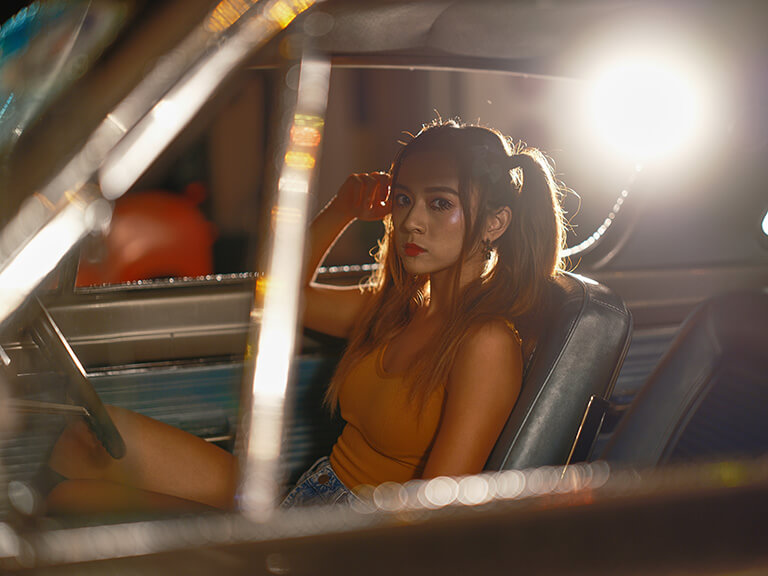 Young woman with pigtails sitting in a vintage car, backlit by a bright light, photographed with the Fujifilm GFX100s