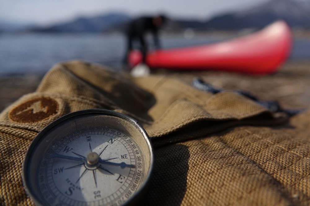 Lifestyle photo of a compass with a kayak in the background