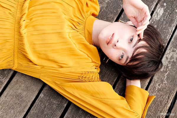 Close-up of woman in elegant yellow dress lying on a weathered timber deck, photographed with the Panasonic LUMIX S 85mm f1.8