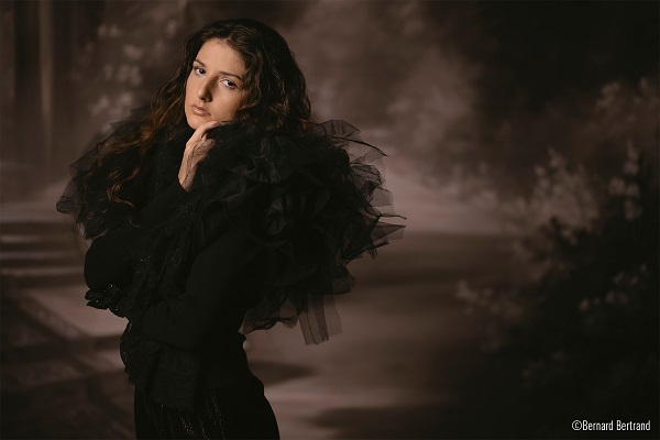 Woman in frilly black outfit posing against a sepia backdrop depicting a garden, shot with Panasonic LUMIX S 85mm f1.8 lens