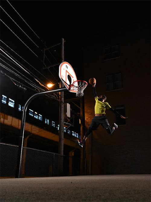 Airborne basketballer about to slam dunk the side a train track at night - shot with Nikon D780