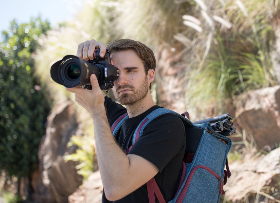 man with a blue backpack taking pictures using nikon dslr